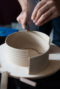 Closeup image of a ceramic artist making test tile in ceramic studio, using white clay and cutting a leather-hard thrown vessel into tile pieces.