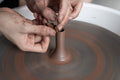 A closeup image of ceramic artist from Singapore based pottery brand, &natural, throwing a teapot spout for Tree Collection, one of the studio’s signature teaware collection, with brown clay.